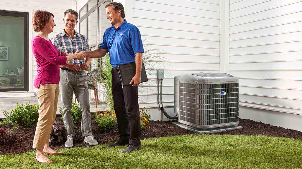 Climate Works Carrier technician greeting homeowners beside a Carrier heat pump outdoor unit