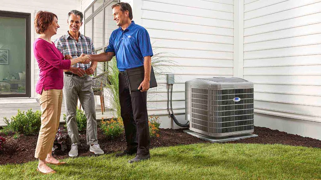 Climate Works Carrier technician greeting homeowners beside a Carrier heat pump outdoor unit